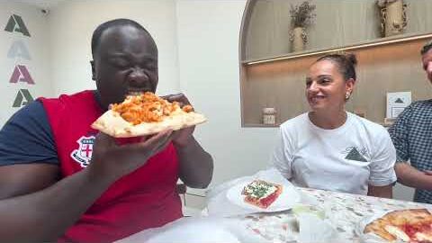 A guest biting into a loaded slice at a table inside Strictly Pizza